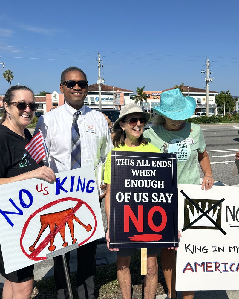 Victor Arias standing with constituents holding hand-painted signs at a community rally to defend democracy in Southwest Florida